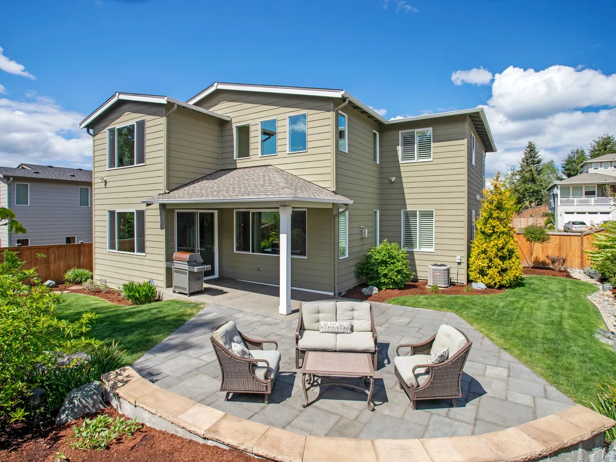 A paver patio with cushioned seating at the back of a house, a wood fence around the yard