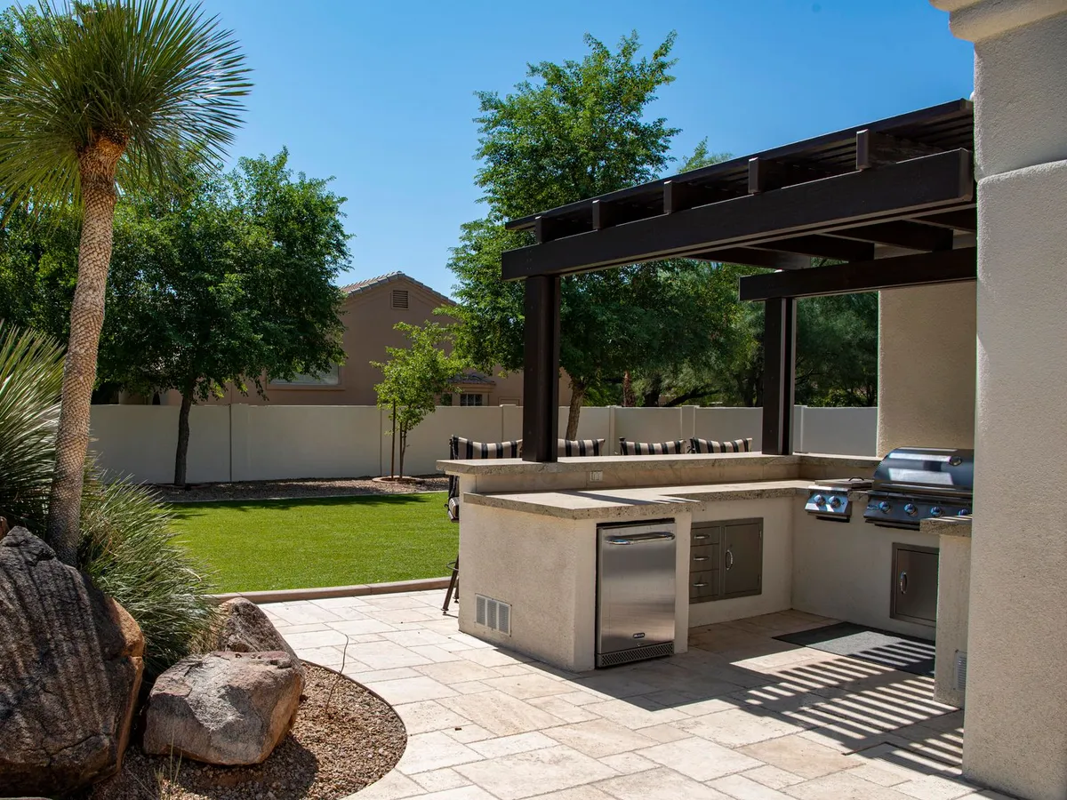 A pergola over a paver patio with a built in outdoor kitchen and grill