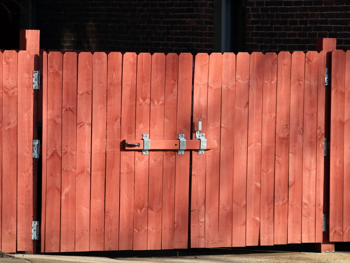 A pair of stained wood gates with a metal latch bar, set in a matching board fence